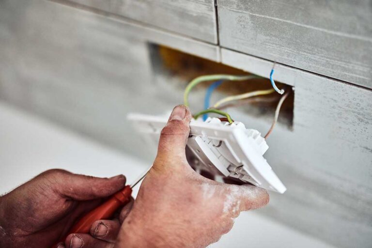 A person inspecting a circuit breaker panel with a flashlight in a residential basement.