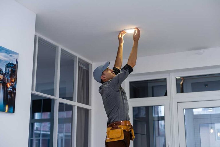 A homeowner clearing storage boxes from in front of an electrical breaker panel in a basement laundry area.